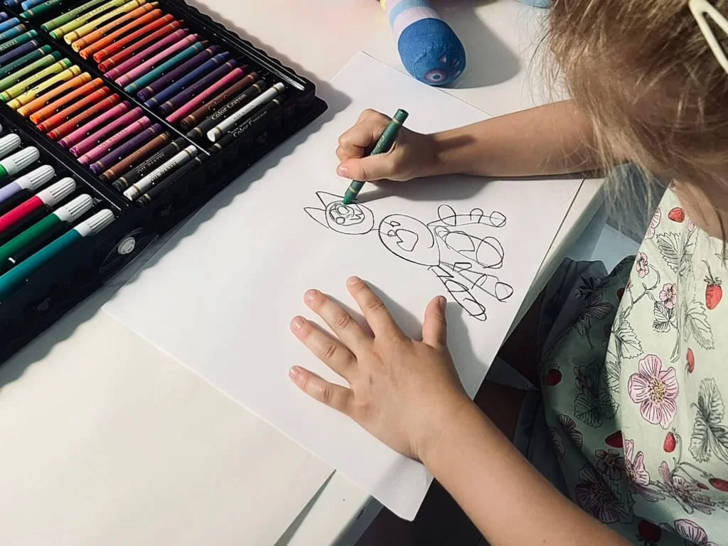 Dziecko rysuje flamastrem przy otwartym zestawie kredek